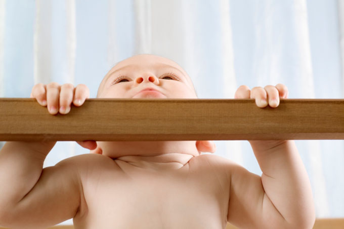 Infant child holding himself up in wooden cot